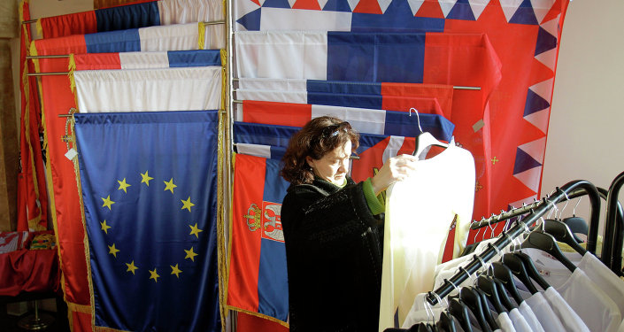 In this photo taken Wednesday, Dec. 7, 2011, a woman looks at an item of clothing in a shop as she stands next to a European Union flag and Serbian flags, in Belgrade, Serbia
